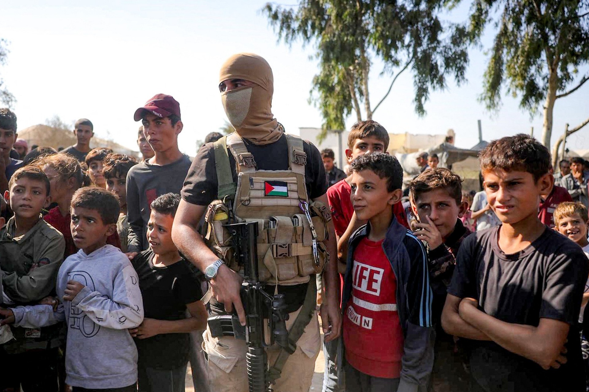 Un miembro enmascarado del ala militar de Hamás hace guardia junto a niños en el sur de Deir el-Balah, en el centro de la Franja de Gaza, el 13 de octubre de 2025. Foto: Bashar Taleb / AFP