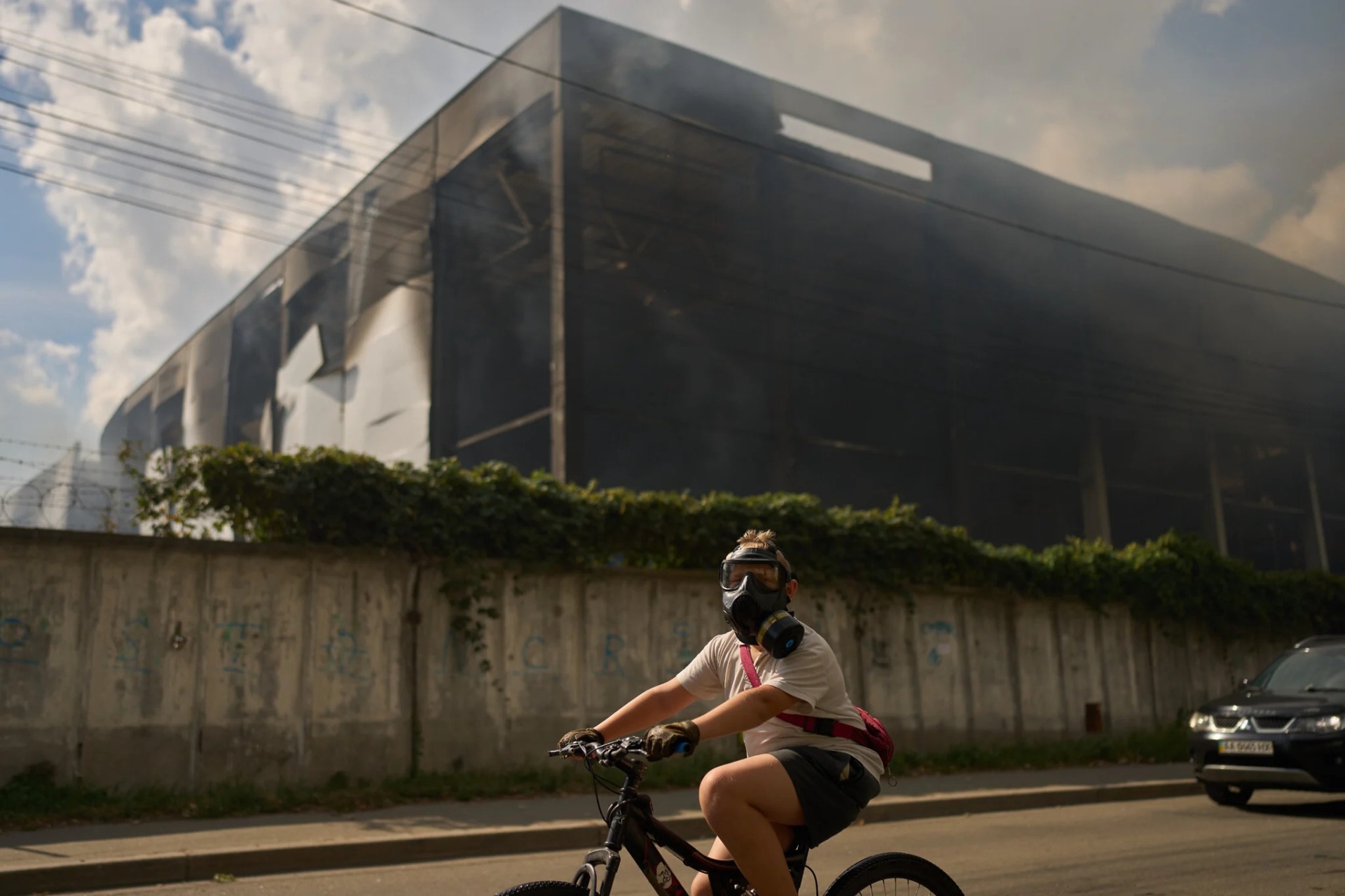 Un residente local utiliza una máscara de gas mientras circula en bicicleta junto a un almacén parcialmente destruido tras un ataque con drones rusos en Brovary, en las afueras de Kiev, Ucrania, el 4 de septiembre de 2026. Foto: AP Photo/Francisco Seco.